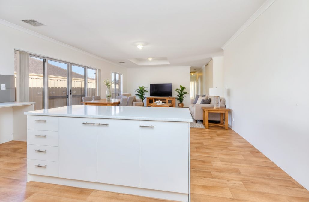 Open-plan kitchen, dining and living area with a large island bench, timber-look floors and sliding doors to outside